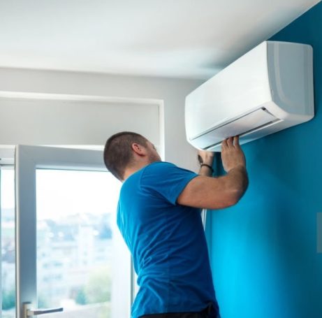 Technicien installant un climatiseur sur un mur bleu.